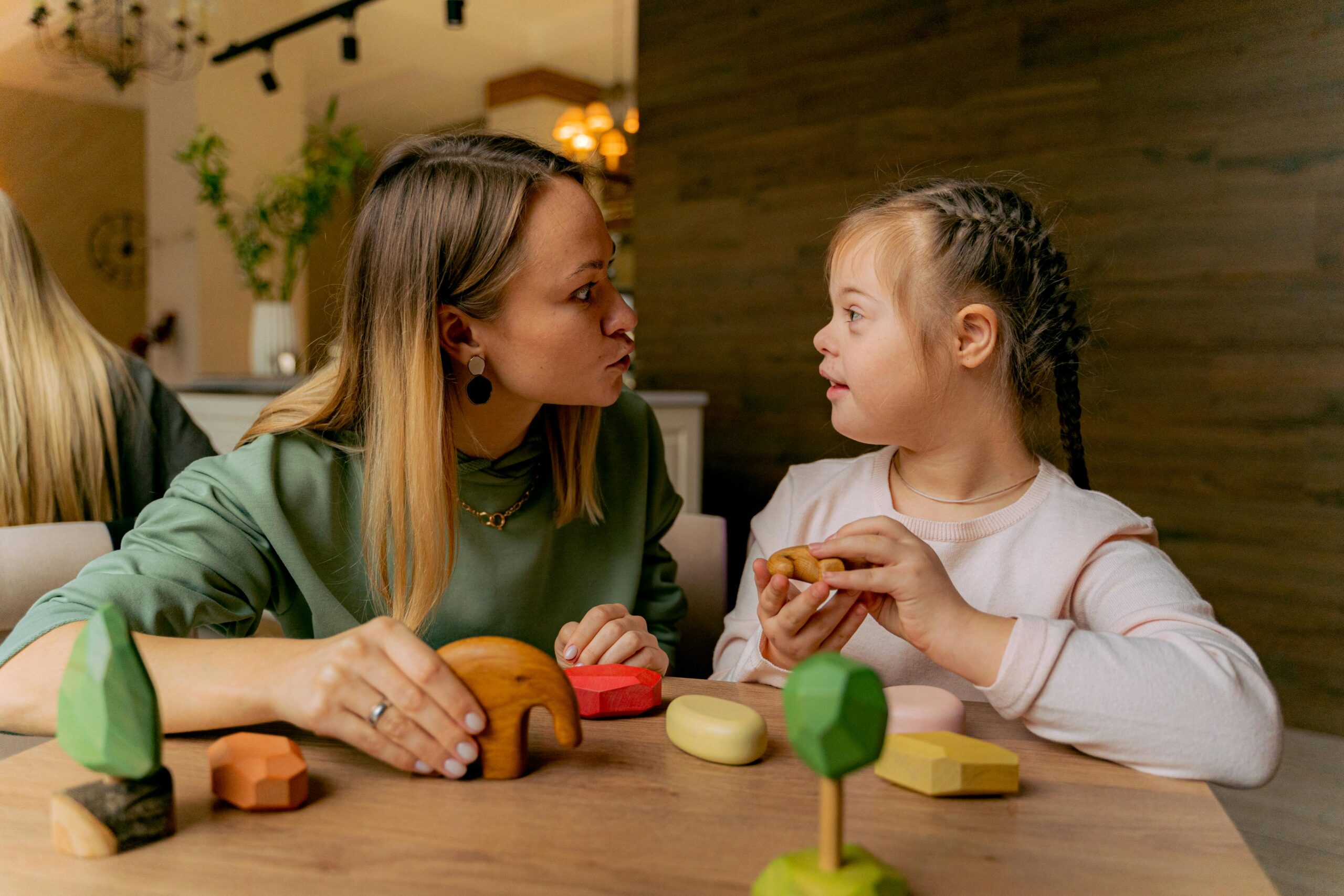 Home An adult woman and a child with Down syndrome engaging in playful interaction with wooden toys indoors.